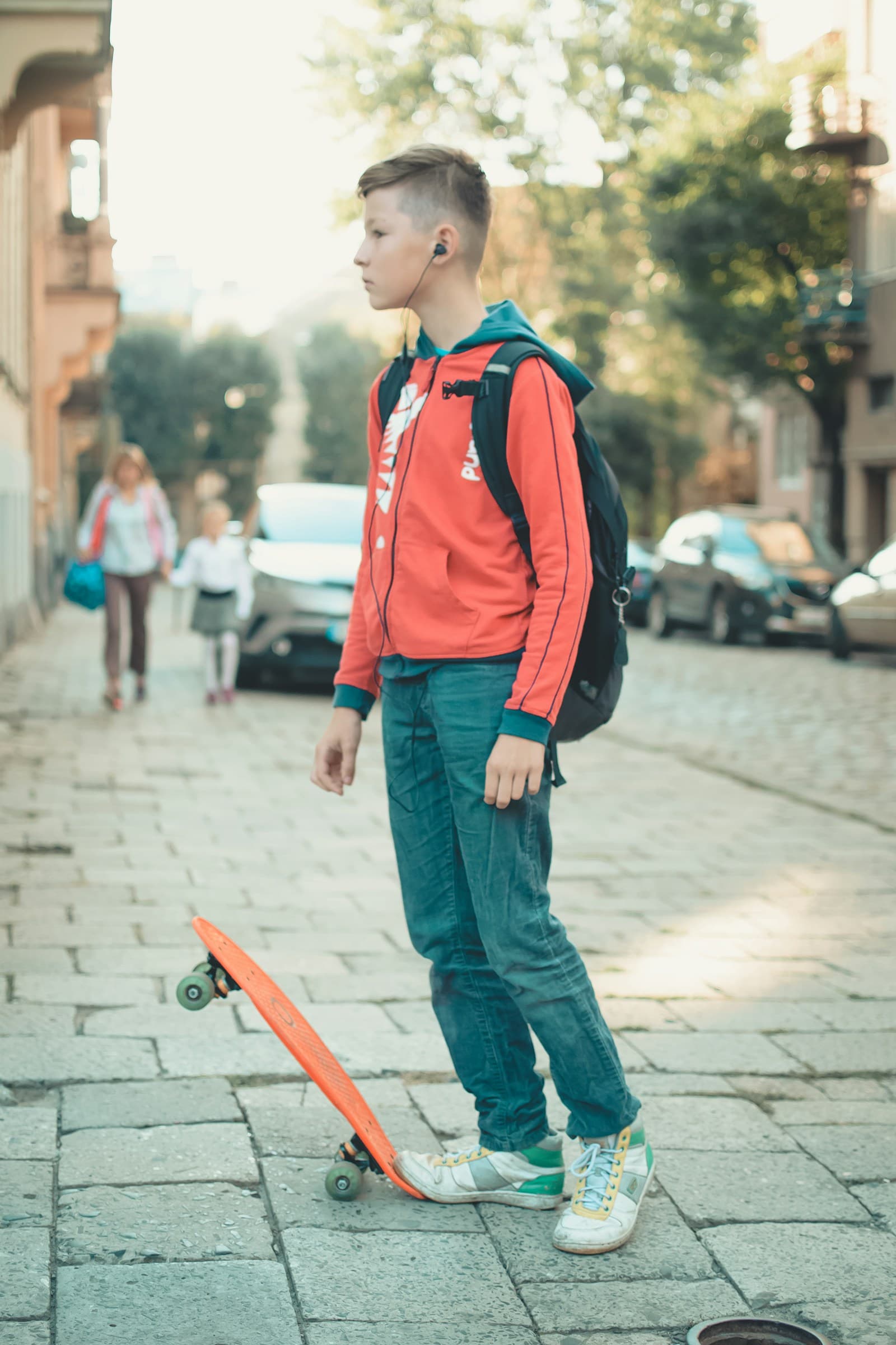 Un adolescent avec un sac à dos et des écouteurs, à côté d'un skateboard.
