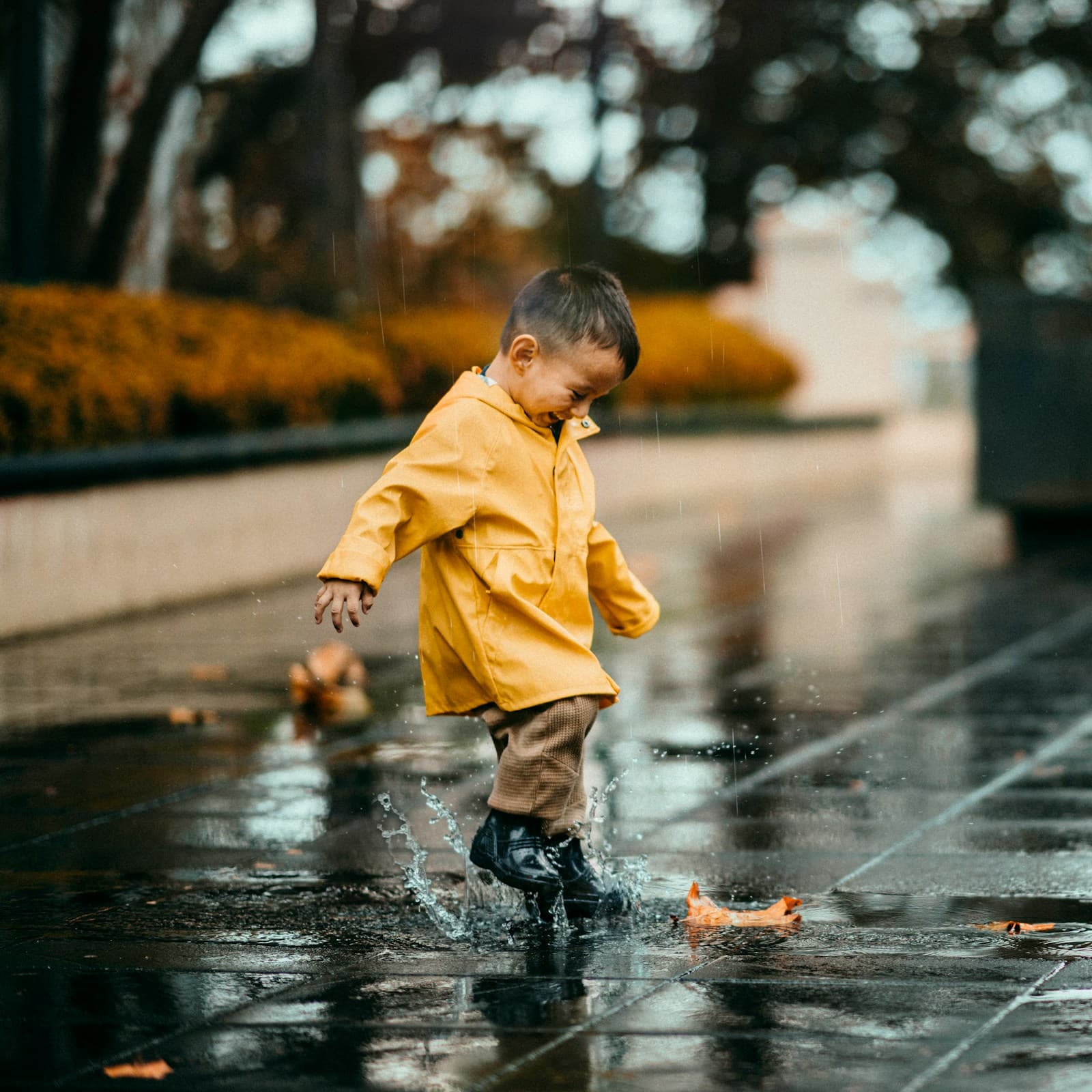 Un enfant en veste à capuche jaune marche sur une route mouillée.