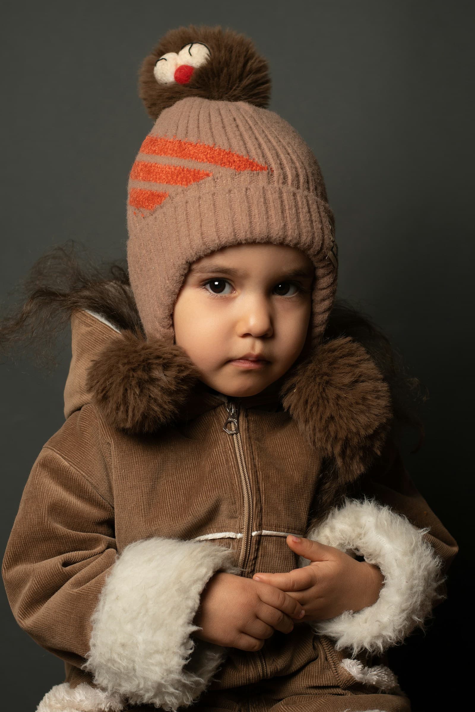 Un jeune enfant porte une veste et un bonnet marron.