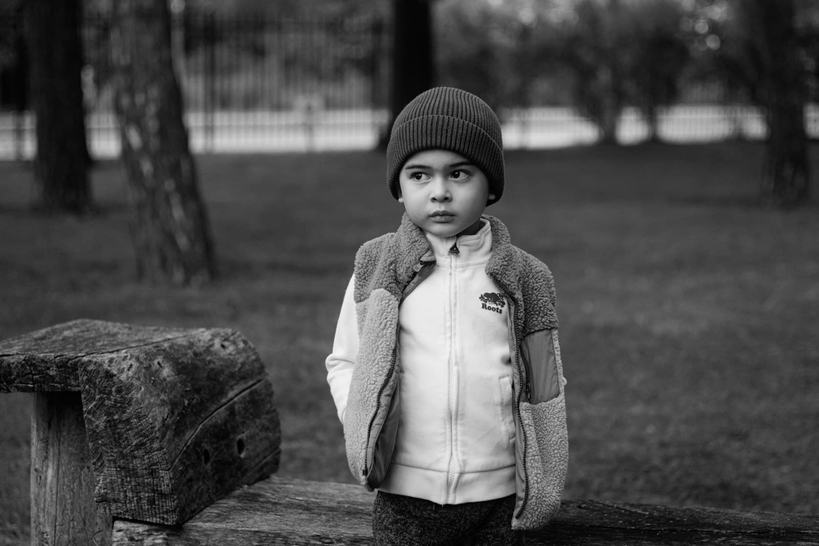 Un garçon en bonnet et gilet sans manches, debout à l'extérieur.