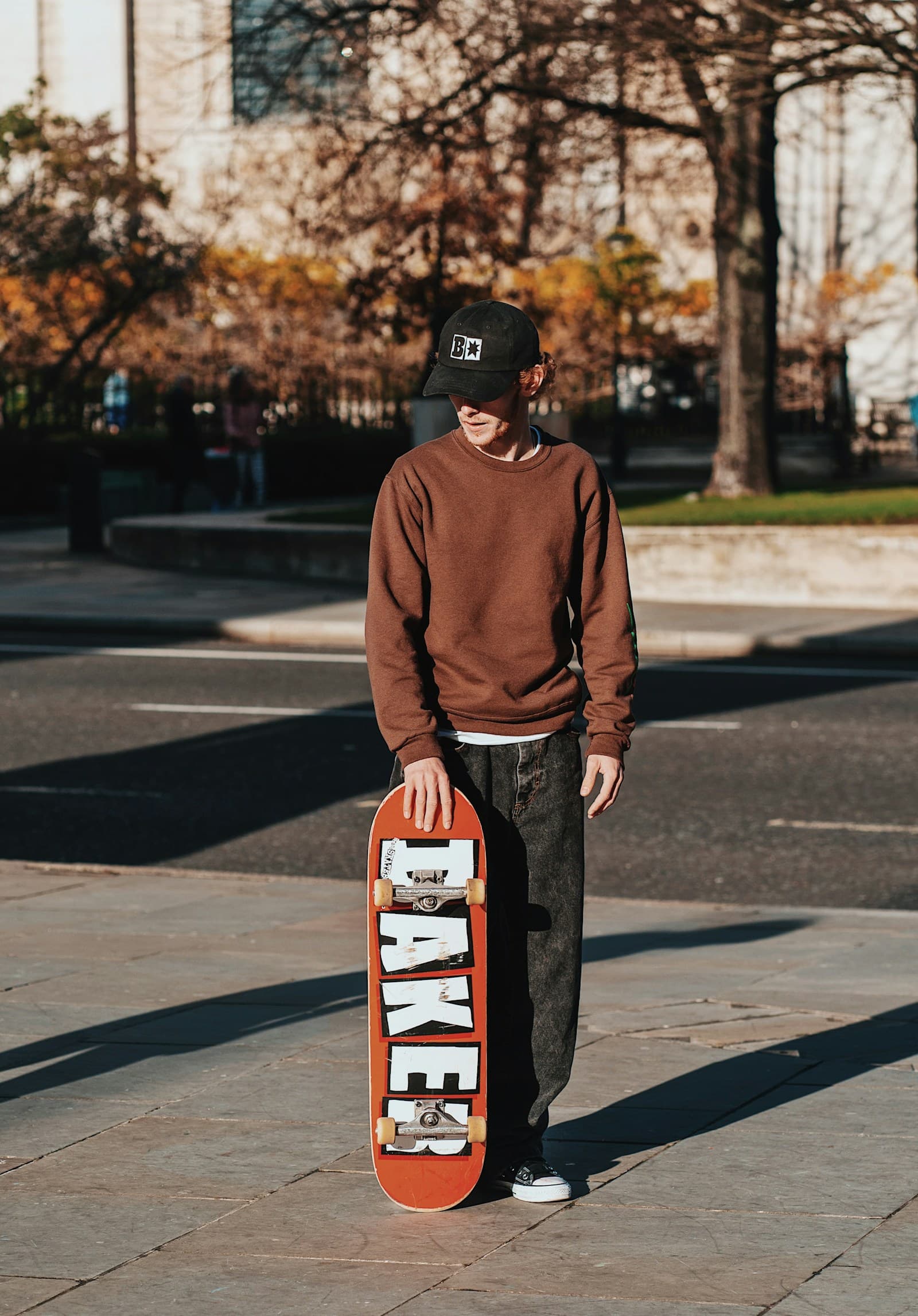 Un adolescent debout sur un trottoir, son skateboard sous le bras.