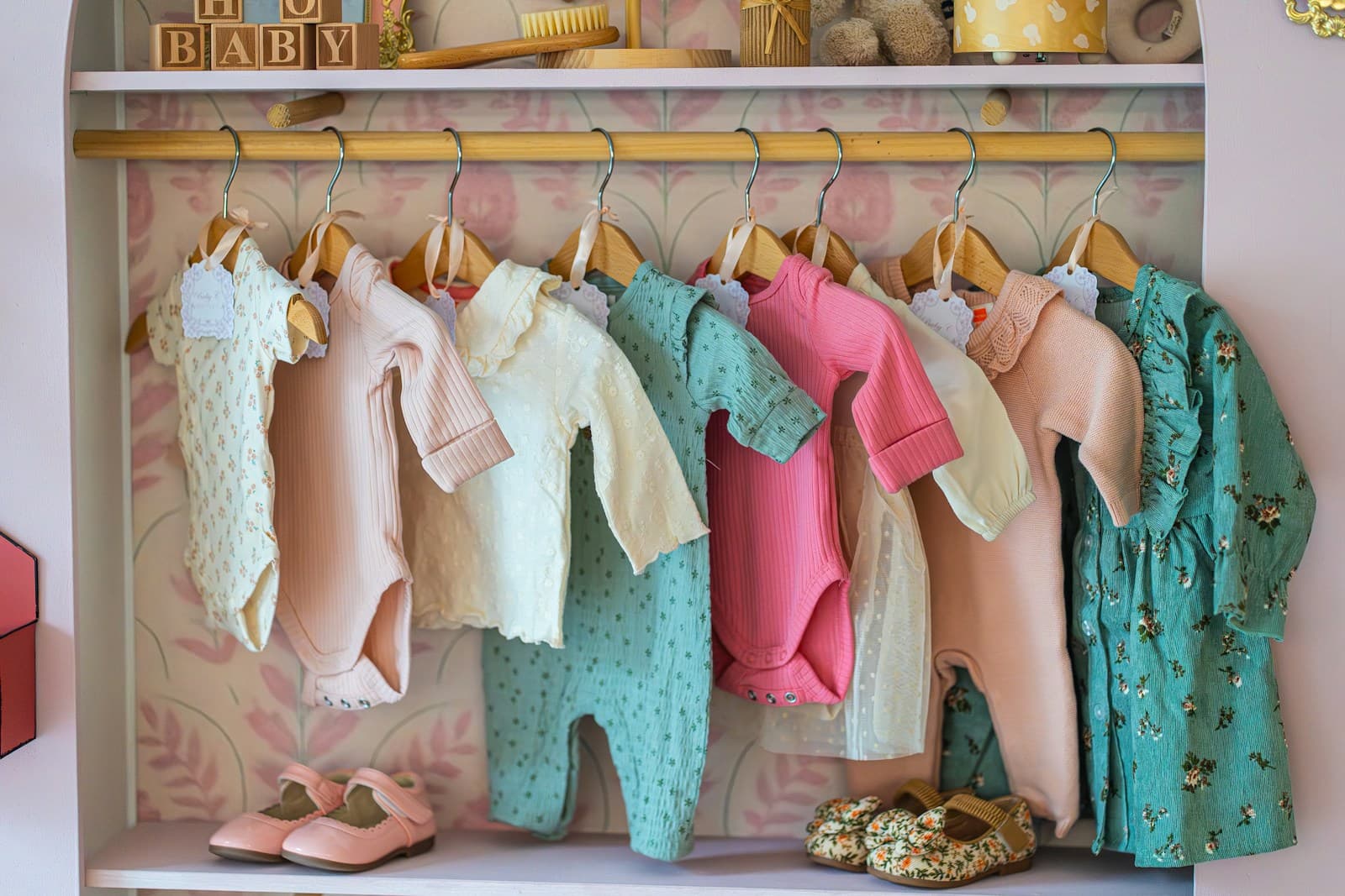 Des vêtements de bébé sur un portant, des chaussures alignées en dessous.