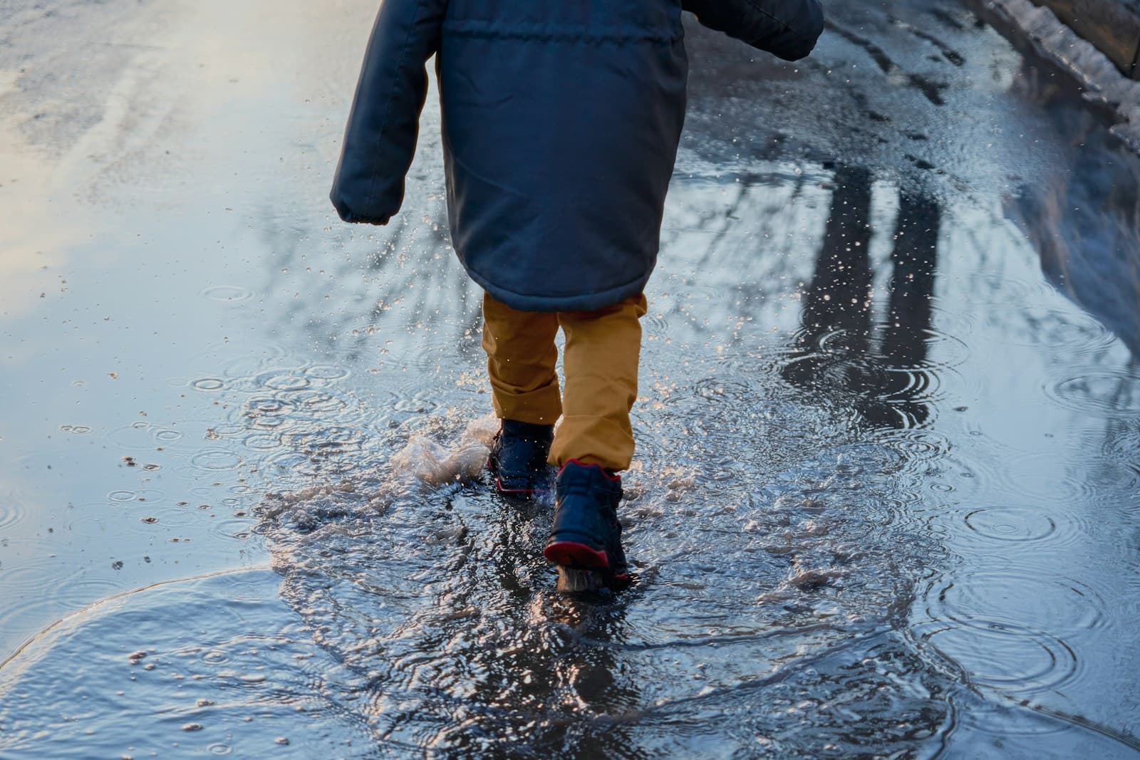 Un enfant en bottes saute dans une flaque et fait gicler l'eau.