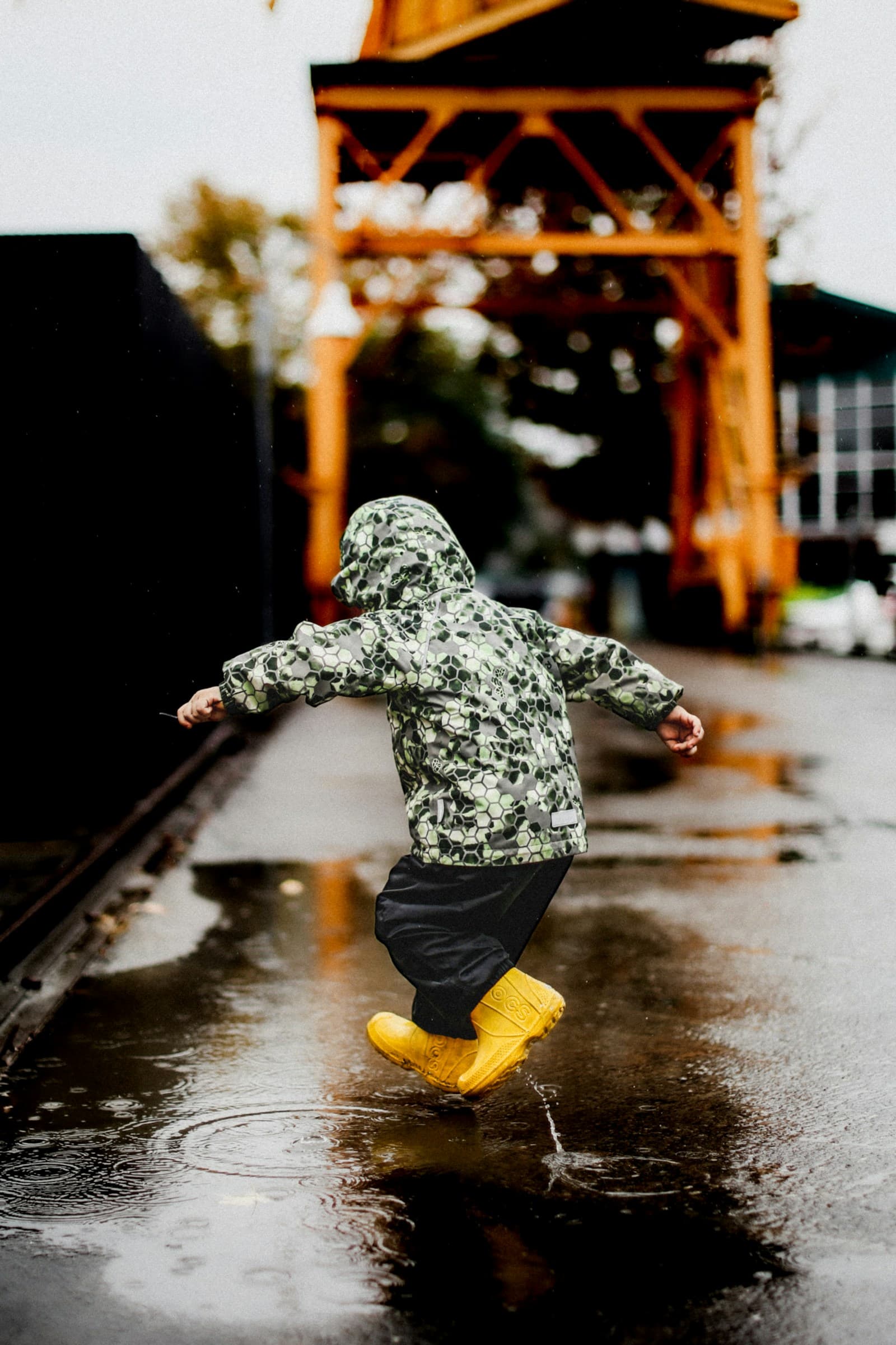 Un enfant saute dans une flaque, sous la pluie.